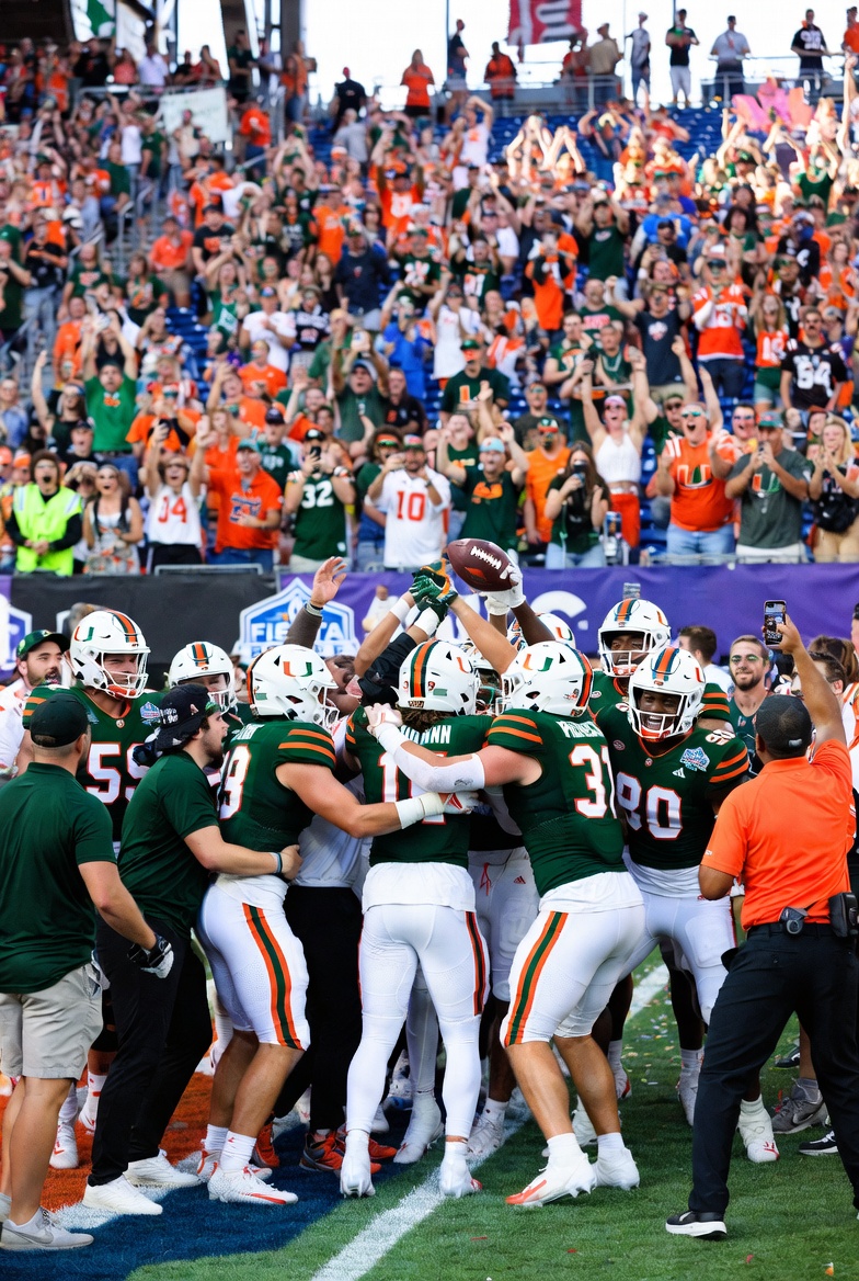 Miami Hurricanes players celebrate their 31-27 victory over Ole Miss Rebels in the 2026 Fiesta Bowl, with team huddle, raised arms, and confetti at State Farm Stadium. (Miami Hurricanes vs Ole Miss Rebels Fiesta Bowl 2026)